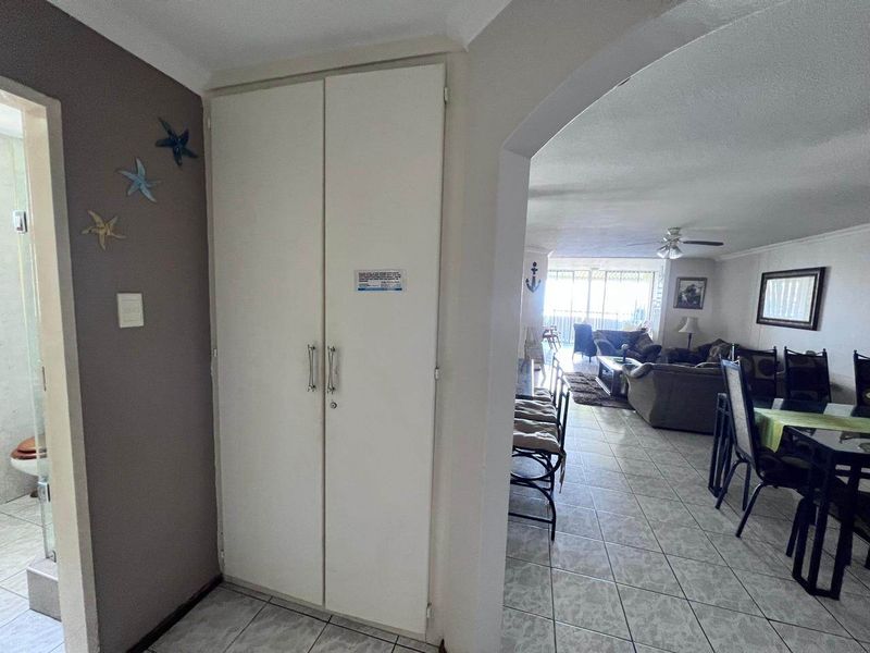 A hallway area featuring a built-in storage cupboard and tiled flooring, providing access to the adjacent living space through an arched entryway.