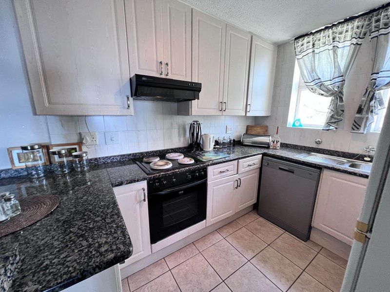 A functional kitchen featuring granite countertops, built-in cabinetry, an electric oven with hob, extractor fan, and tiled flooring.