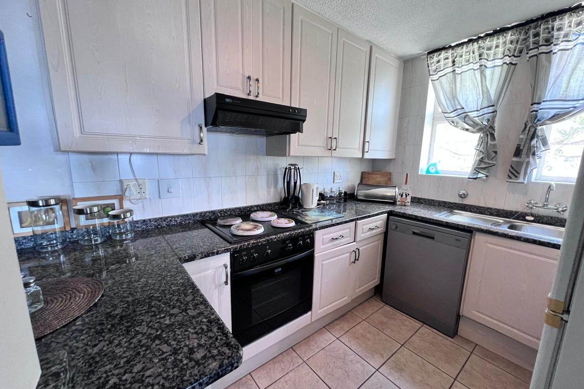 A functional kitchen featuring granite countertops, built-in cabinetry, an electric hob with extractor fan, and tiled flooring.