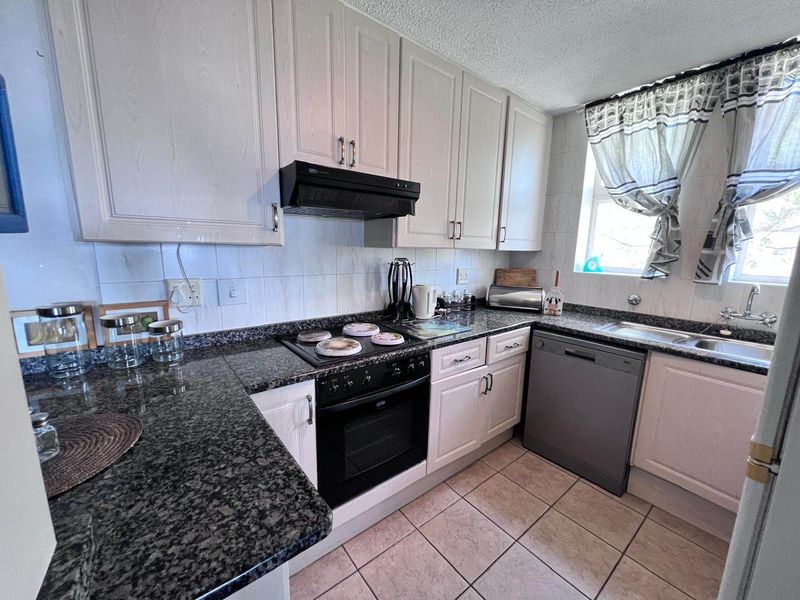 A functional kitchen featuring granite countertops, built-in cabinetry, an electric hob with extractor fan, and tiled flooring.
