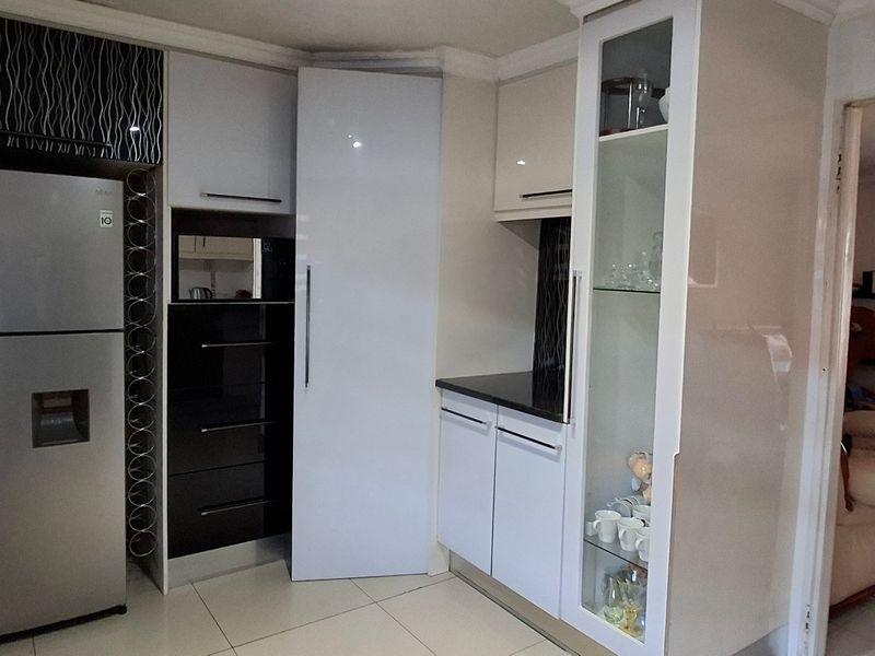 A modern kitchen featuring high-gloss cabinetry, black stone countertops, and a built-in glass display cabinet, with tiled flooring throughout.