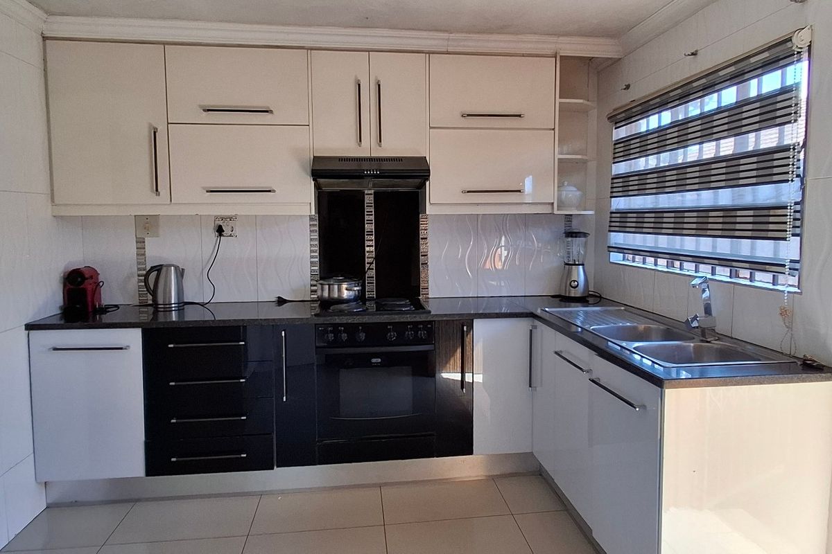 A functional kitchen featuring high-contrast black and white cabinetry, granite countertops, a built-in oven with extractor fan, and tiled finishes throughout.