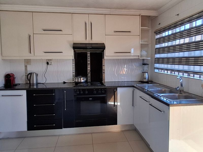 A functional kitchen featuring high-contrast black and white cabinetry, granite countertops, a built-in oven with extractor fan, and tiled finishes throughout.
