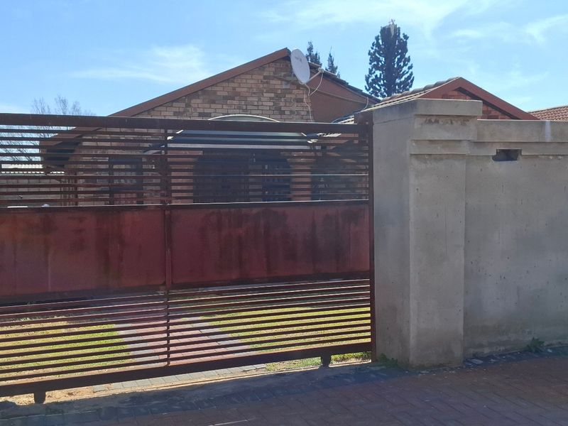 Front view of a residential property featuring a brick facade, tiled roof, and a metal sliding gate with a surrounding boundary wall.