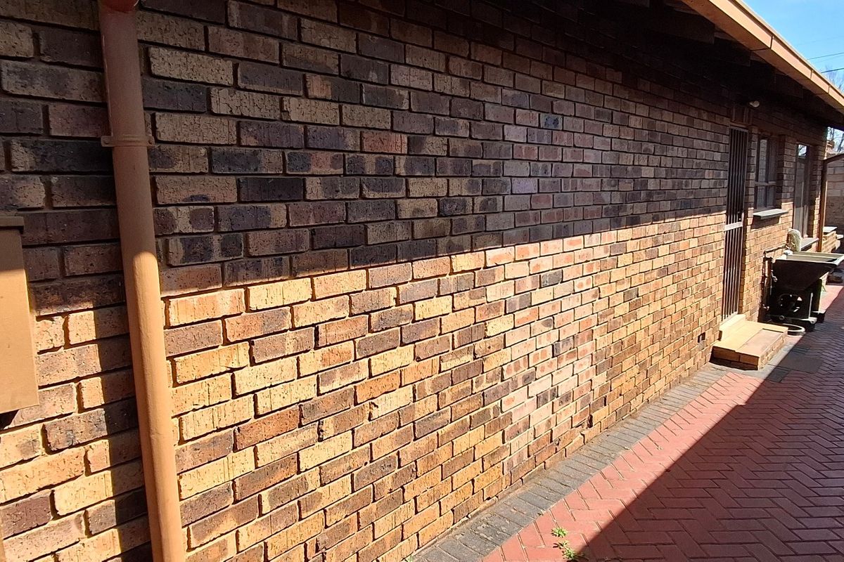 A side exterior view of the property featuring a face brick wall, paved walkway, and secure access point.