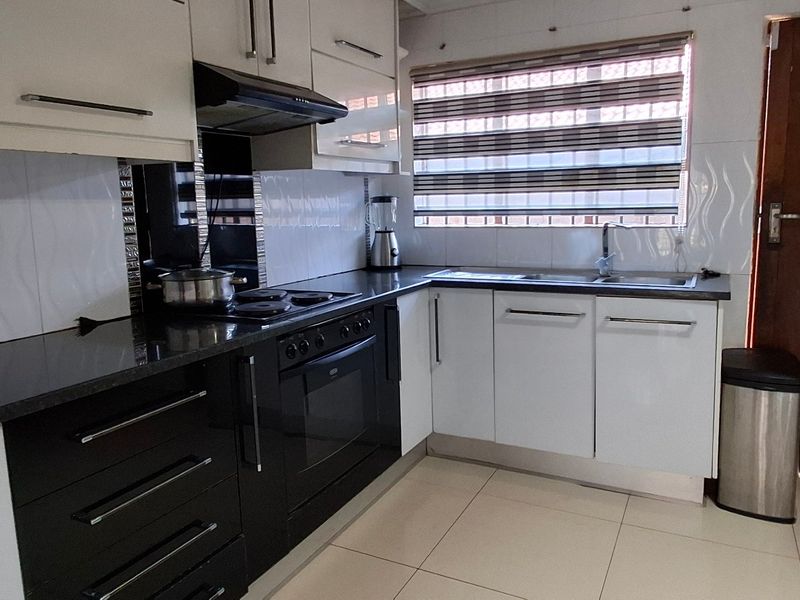 A modern kitchen featuring high-gloss cabinetry, granite countertops, built-in oven and hob, and tiled finishes throughout.