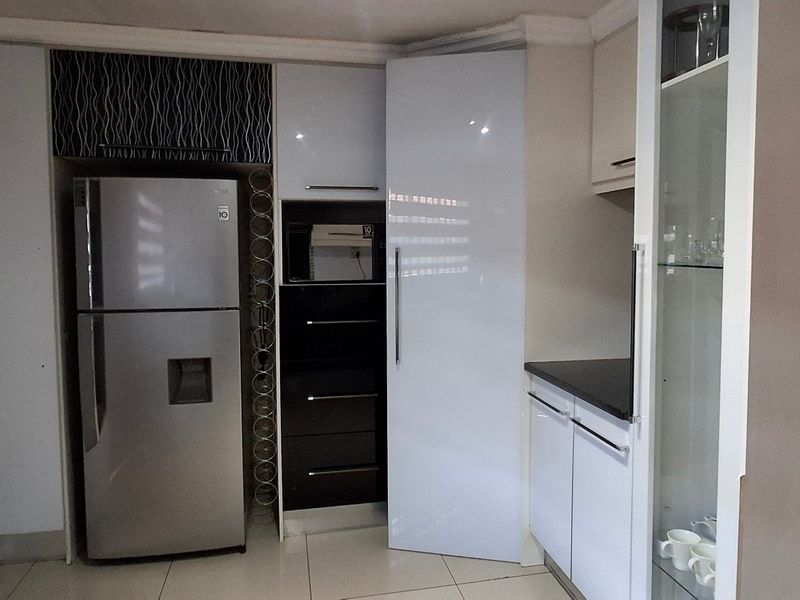 A compact kitchen area featuring modern white cabinetry, dark stone countertops, tiled flooring, and dedicated space for a refrigerator and built-in microwave.