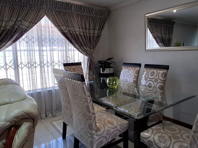 A dining room area featuring tiled flooring and a window fitted with a security gate and curtain rails.