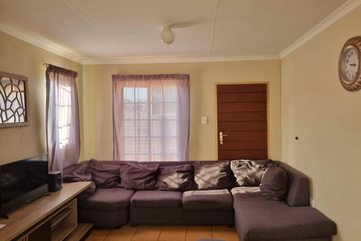 A living room featuring tiled flooring, a sliding glass door providing natural light, and a wooden door leading to an adjacent space.