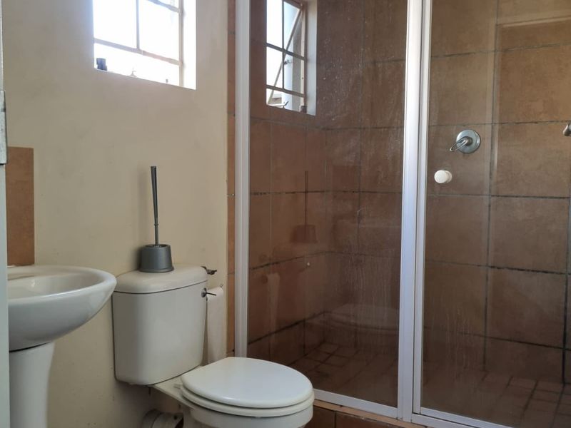 A functional bathroom featuring a pedestal basin, toilet, and a glass-enclosed shower with tiled finishes.