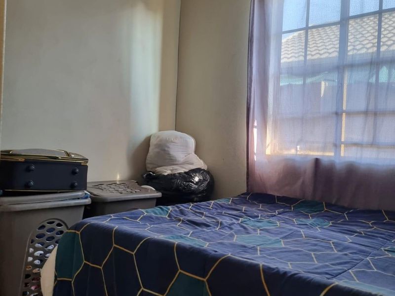 A bedroom featuring tiled flooring and a window with security bars, providing natural light and a functional layout.