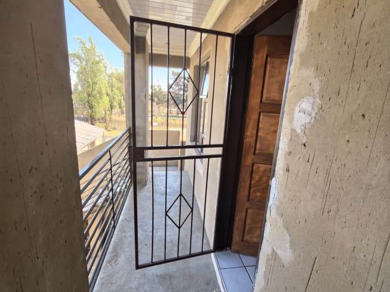 A covered balcony area featuring a security gate, timber door, and metal balustrade, currently requiring finishing work on the wall surfaces.