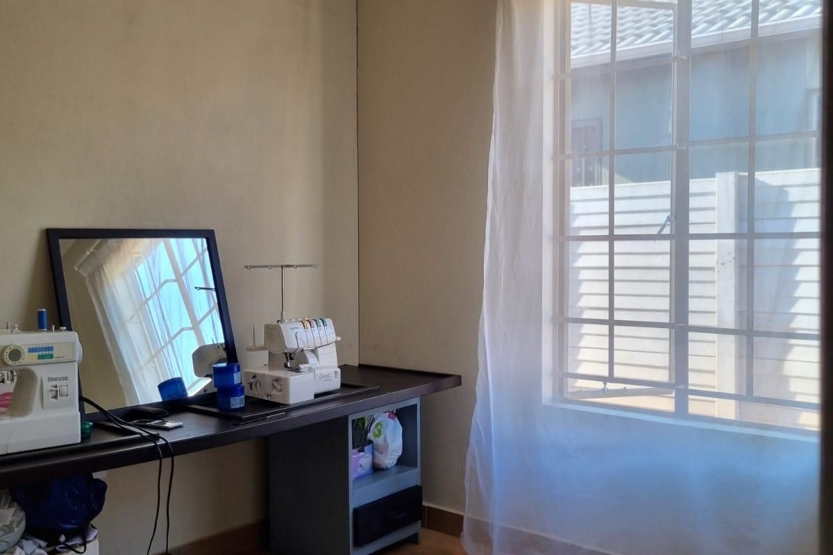 A functional bedroom featuring tiled flooring, a window with security bars, and neutral wall finishes, suitable for use as a bedroom or home office.