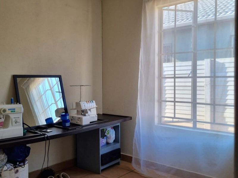 A functional bedroom featuring tiled flooring, a window with security bars, and neutral wall finishes, suitable for use as a bedroom or home office.
