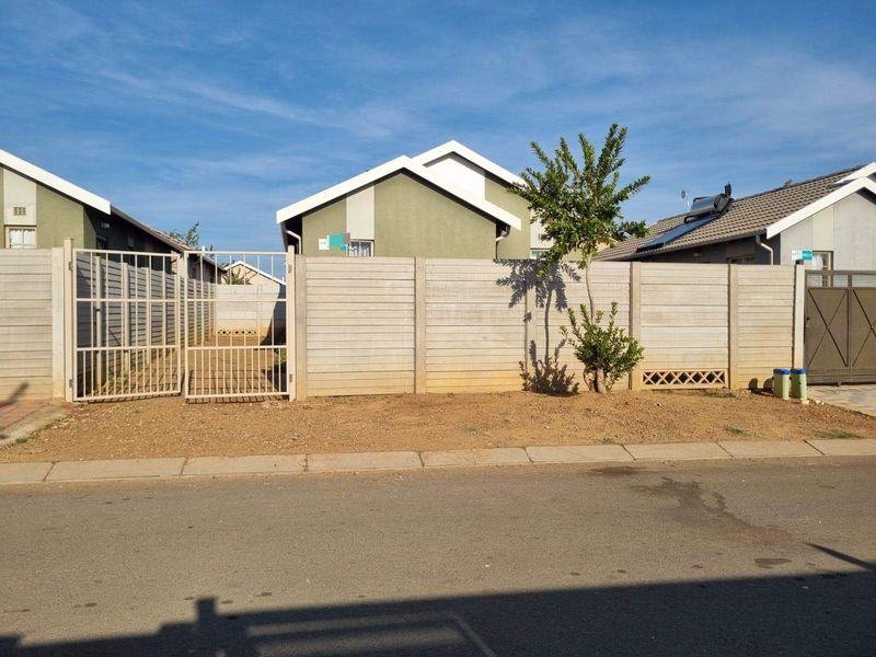 Front view of the property featuring a precast concrete boundary wall, metal gate, and an unlandscaped yard area.