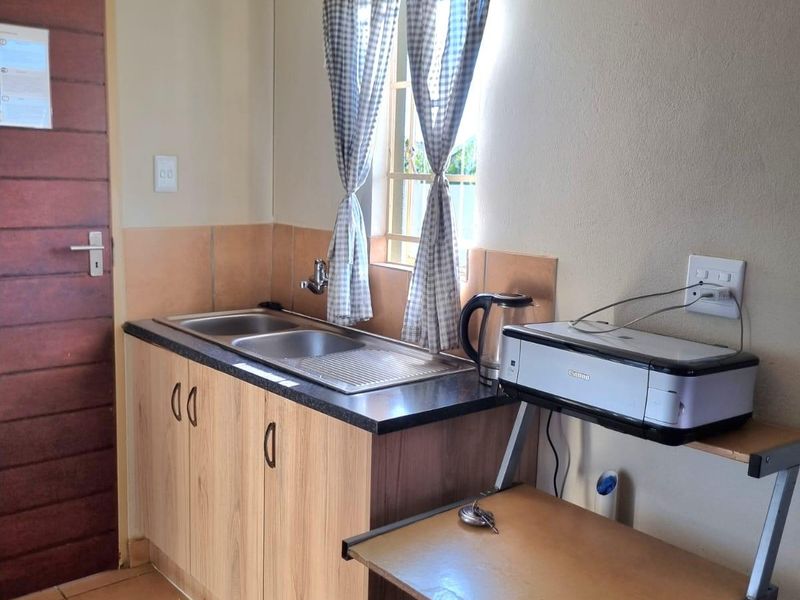 A functional scullery area featuring a stainless steel sink, laminate cabinetry, and tiled splashback, providing a practical space for food preparation and cleaning.