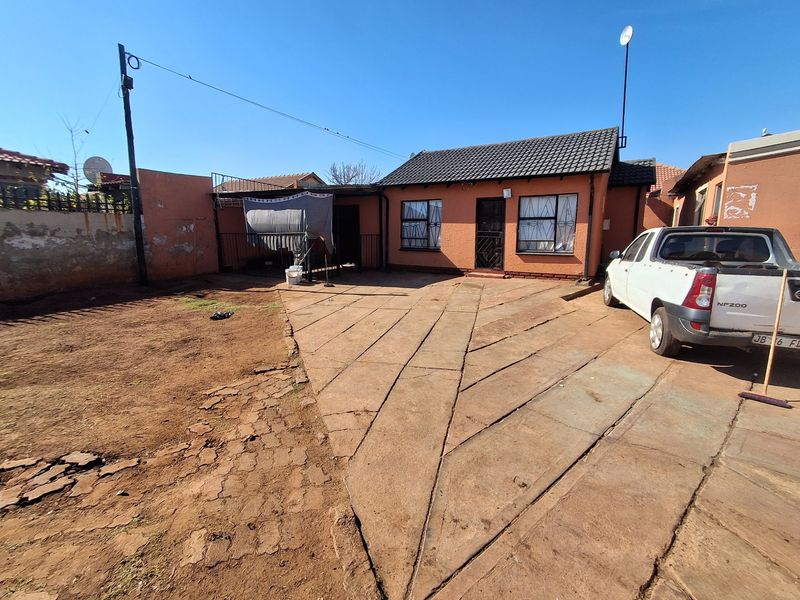 Front exterior view of a single-story house featuring a tiled roof, security bars on windows, and a paved driveway area with a boundary wall.
