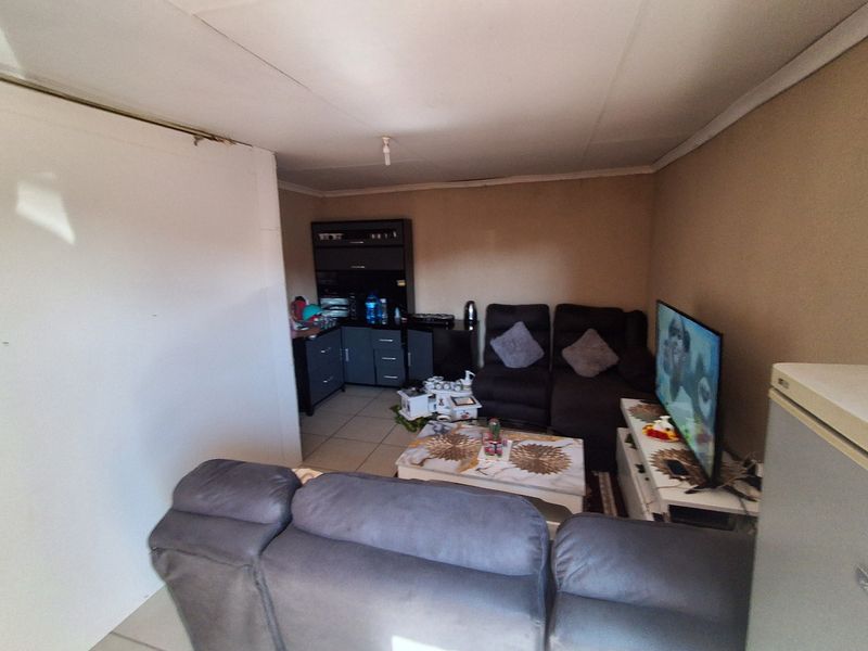 A compact living area featuring tiled flooring and coved ceilings, offering a functional space that could benefit from cosmetic updates and improved lighting.