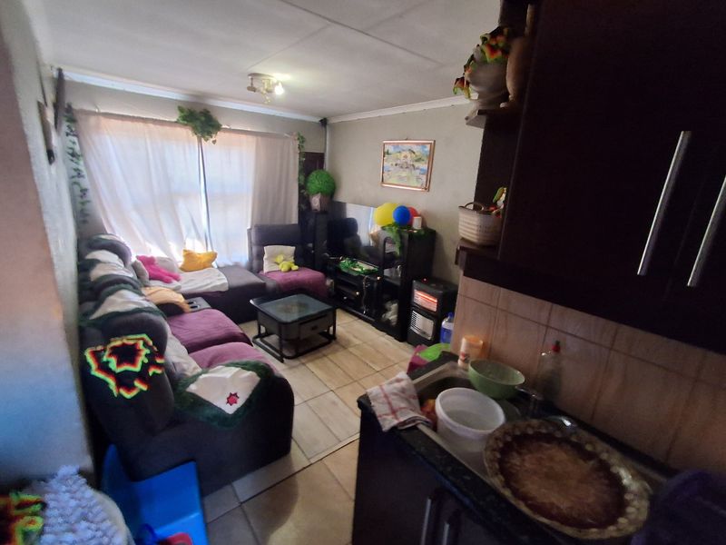An open-plan living area featuring tiled flooring and a compact kitchen space with built-in cabinetry and a sink.