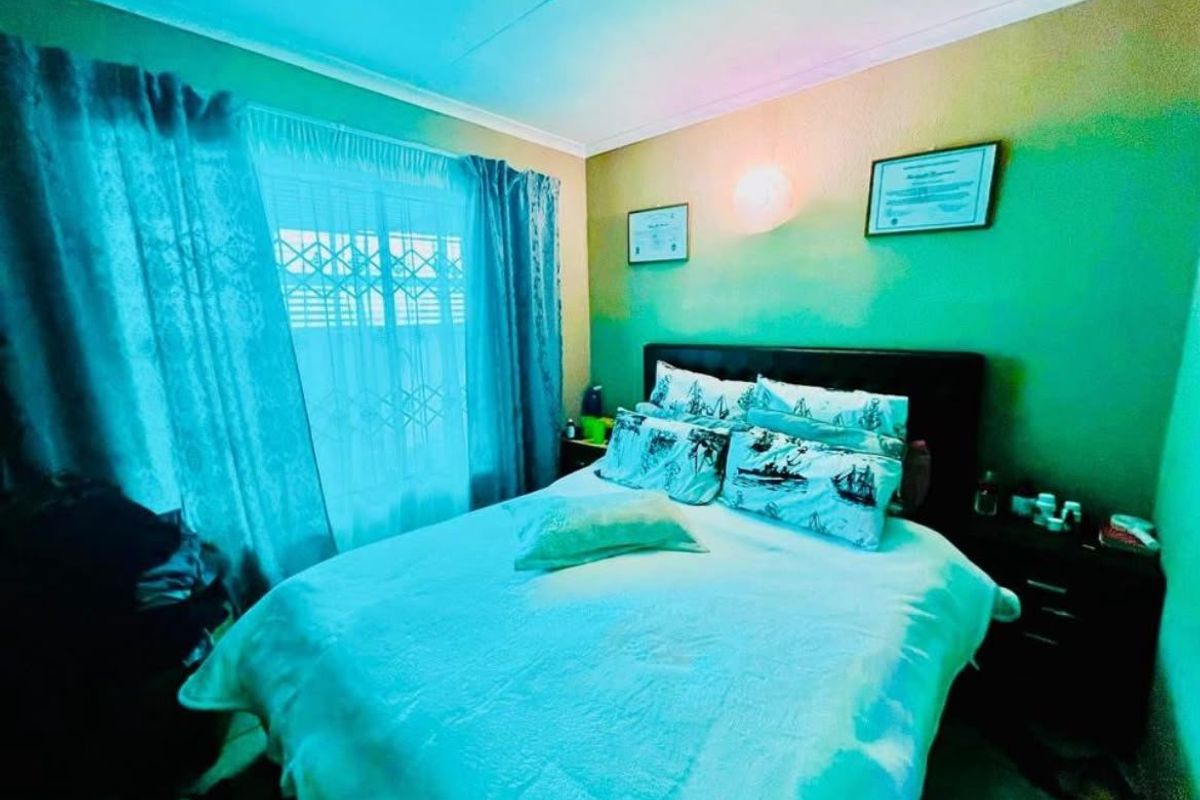 A bedroom featuring a window with a security gate and wall-mounted lighting. The room has a standard layout with neutral wall finishes.