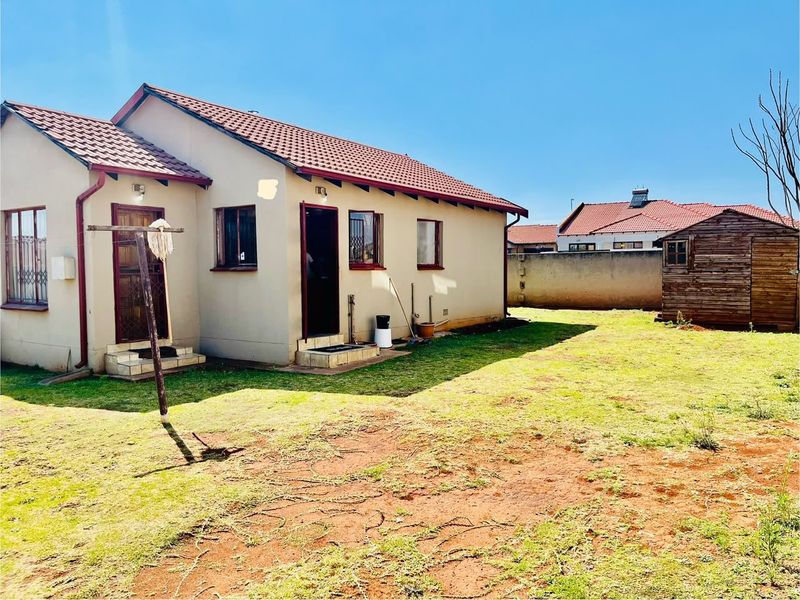 Rear view of the house featuring a tiled roof, security gates, and a spacious backyard with a detached wooden storage shed.