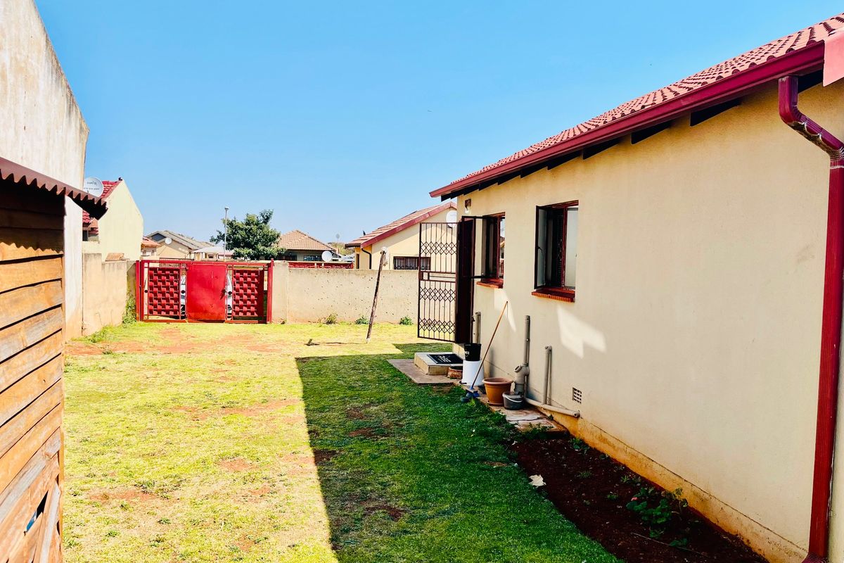 Rear view of the property featuring a private garden, boundary wall, and tiled roof with integrated guttering system.