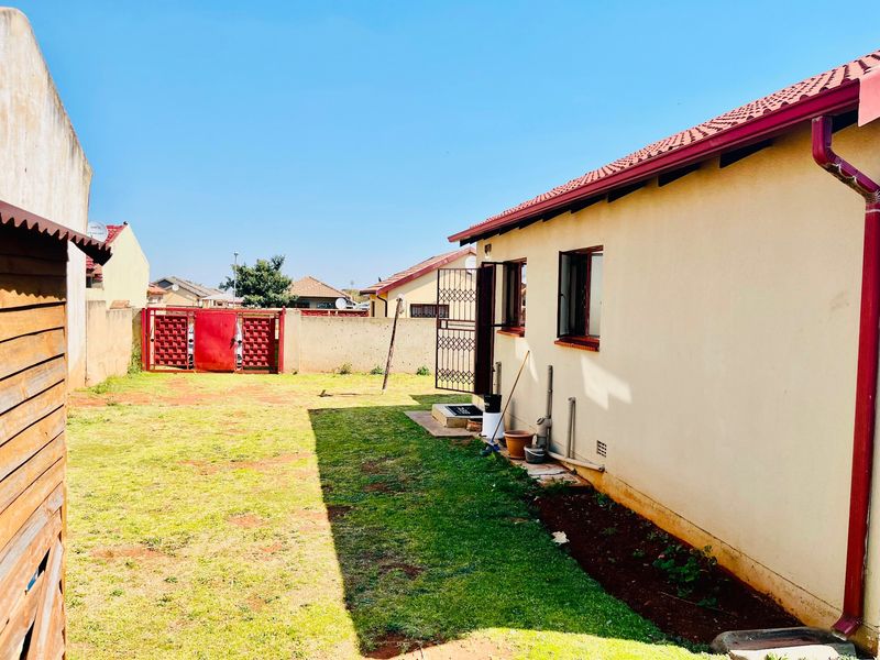Rear view of the property featuring a private garden, boundary wall, and tiled roof with integrated guttering system.