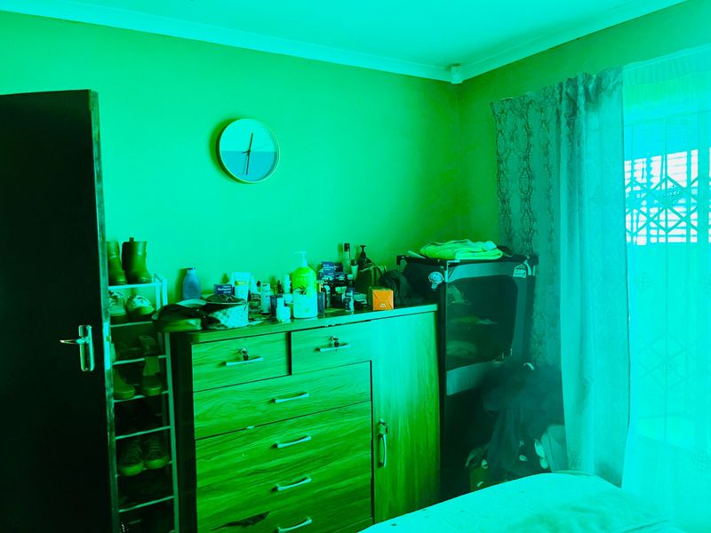 A bedroom interior featuring a window with a security gate and curtain rail, currently heavily affected by a green light cast.