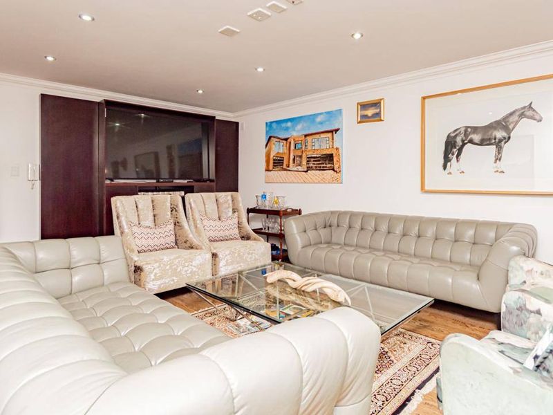 A spacious living room featuring hardwood flooring, recessed downlighting, and custom built-in media cabinetry.