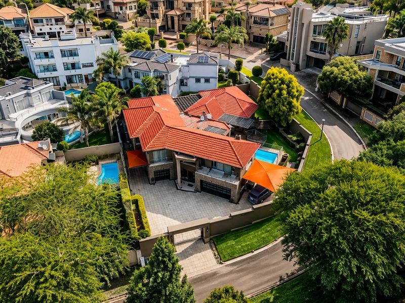 Aerial view of a modern residential property featuring a tiled roof, swimming pool, paved driveway, and secure perimeter wall within a suburban estate.