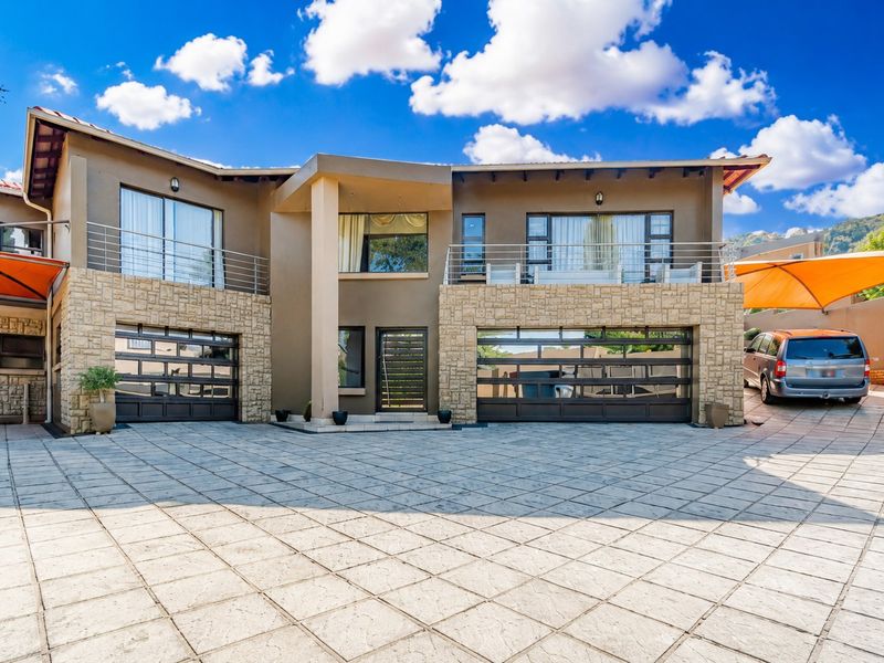 Modern double-story residence featuring stone cladding, a spacious paved driveway, double garage, and upper-level balconies with stainless steel railings.