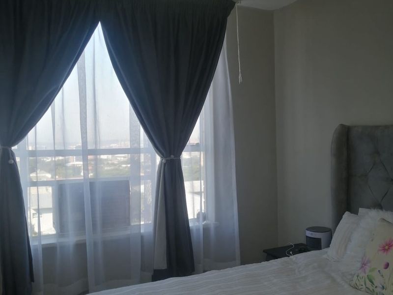 A bedroom featuring a large window with curtains and a central flush mount ceiling light fixture.