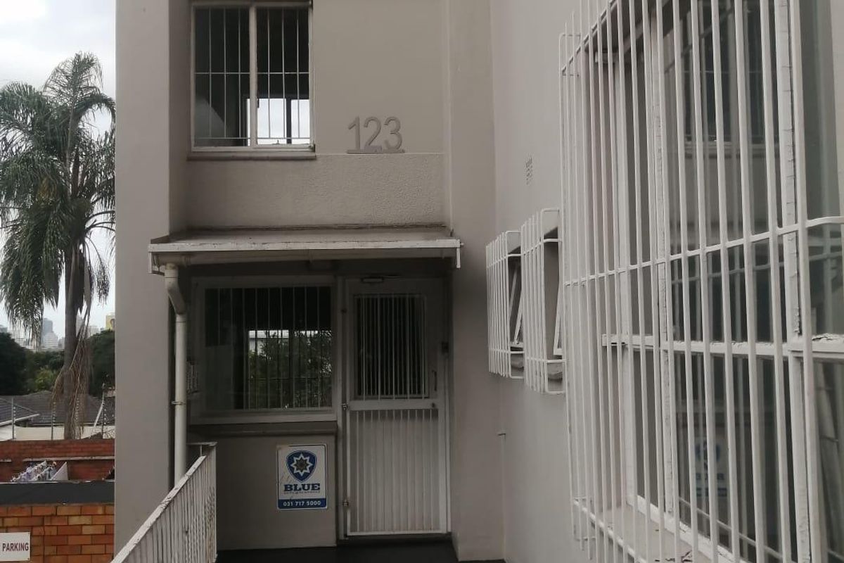 Exterior view of the Manning Hall apartment building entrance, featuring security bars on windows and a secure gated access point.