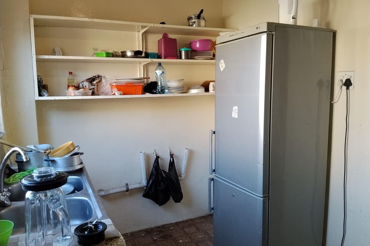 A basic kitchen area featuring a double bowl sink, tiled countertop, and open shelving, requiring significant renovation and modernization of finishes.