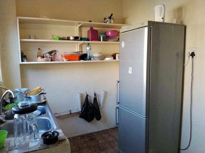A basic kitchen area featuring a double bowl sink, tiled countertop, and open shelving, requiring significant renovation and modernization of finishes.