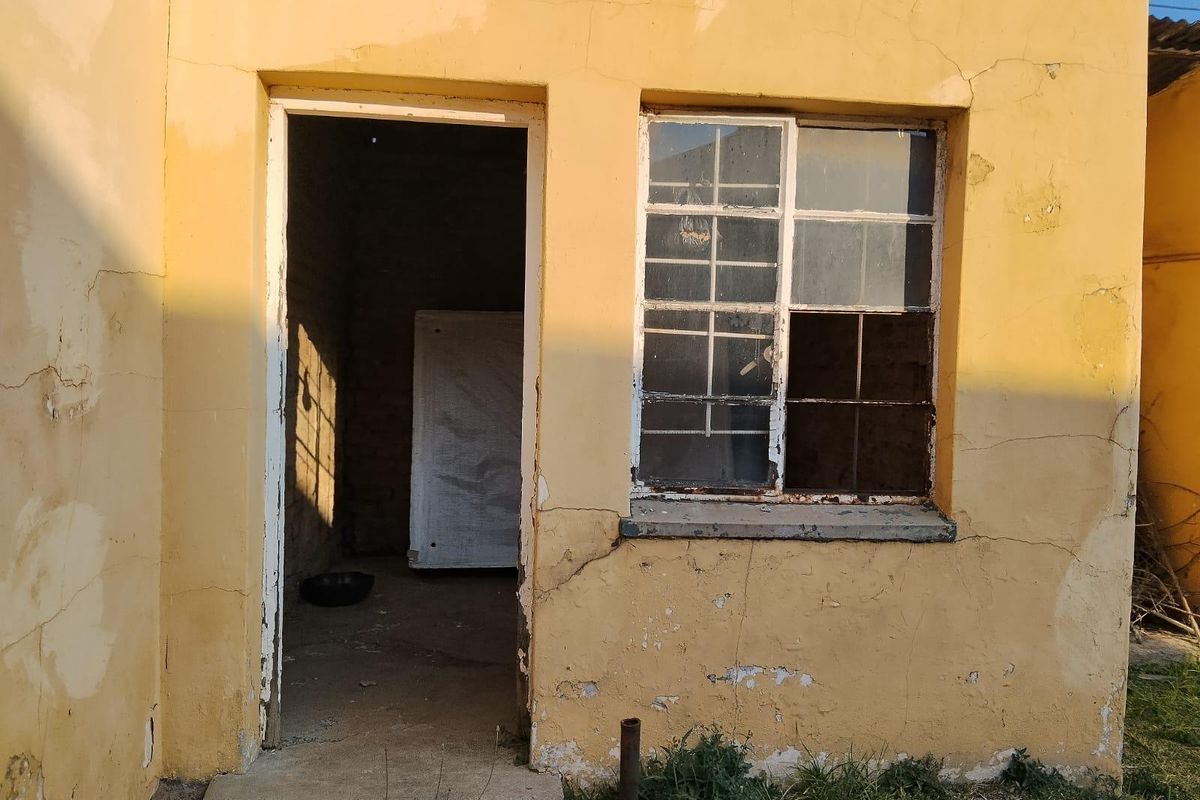 Exterior view of a rear building section showing significant plaster cracking, peeling paint, and a damaged steel-framed window requiring maintenance.