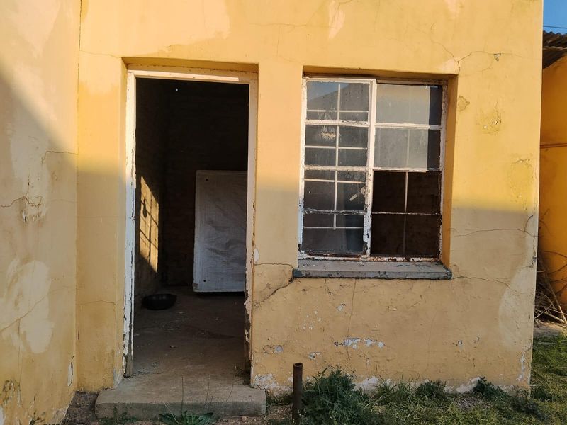 Exterior view of a rear building section showing significant plaster cracking, peeling paint, and a damaged steel-framed window requiring maintenance.