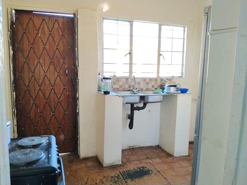 A functional kitchen area featuring a double basin sink, tiled splashback, and direct access to an exterior security door.