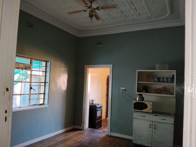 A dated kitchen area featuring original timber flooring, a decorative pressed metal ceiling, and basic built-in cabinetry with a view into an adjacent room.