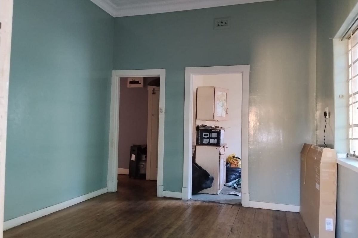 An empty living room featuring original timber flooring, decorative ceiling cornices, and dual doorways leading to adjacent spaces.