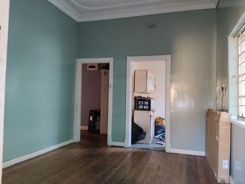 An empty living room featuring original timber flooring, decorative ceiling cornices, and dual doorways leading to adjacent spaces.