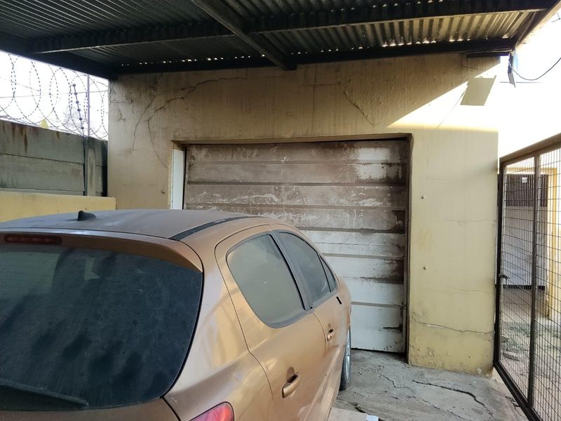 A detached garage structure featuring a corrugated metal roof, concrete flooring, and a weathered garage door with visible exterior wall cracking.