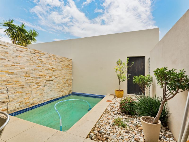 Private courtyard featuring a compact swimming pool with stone cladding feature wall and low-maintenance pebble garden bed.