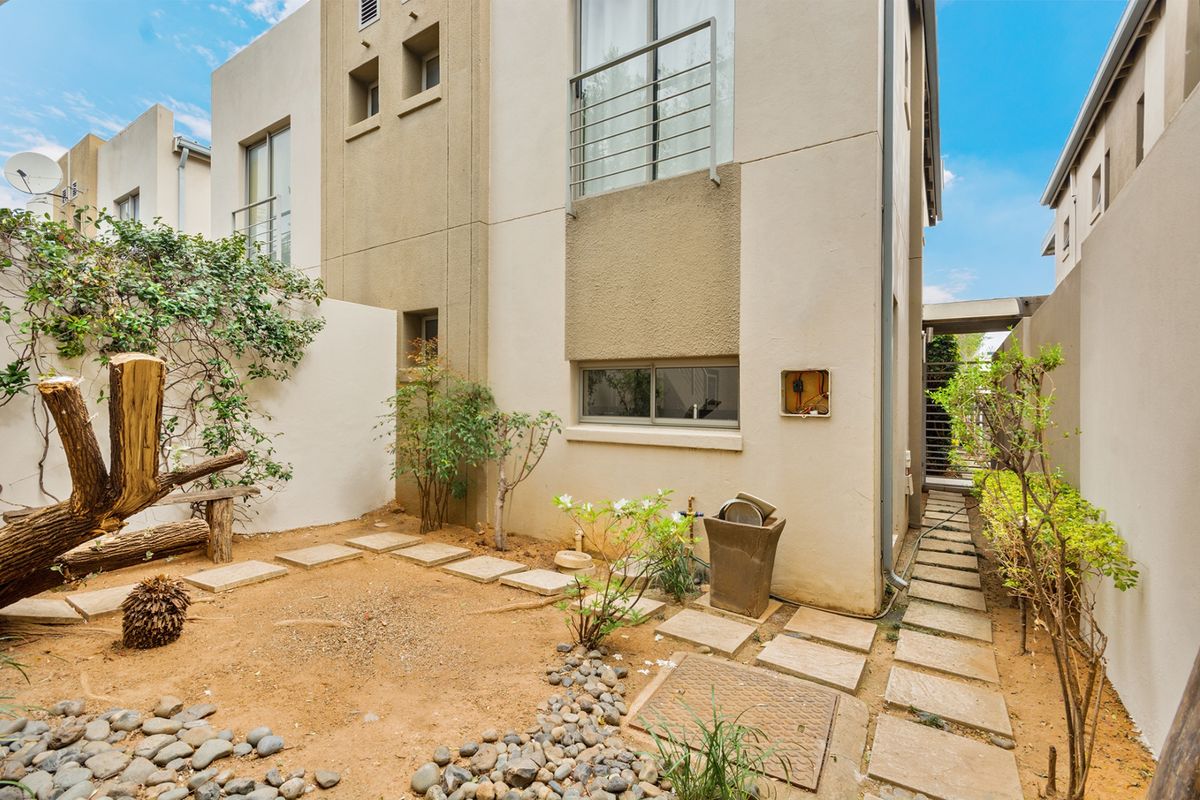 Rear exterior view of a townhouse featuring a small garden area, paved pathways, and a balcony on the upper level.