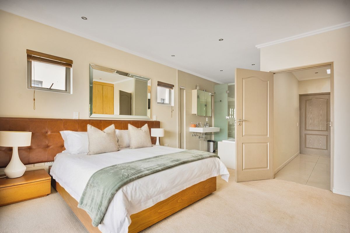 Spacious bedroom featuring neutral carpeting, recessed lighting, and an open-plan en-suite bathroom with a modern vanity and glass-enclosed shower.