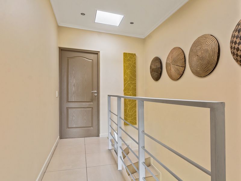 A bright, tiled upper-level hallway featuring a skylight, modern metal balustrade, and neutral wall finishes.