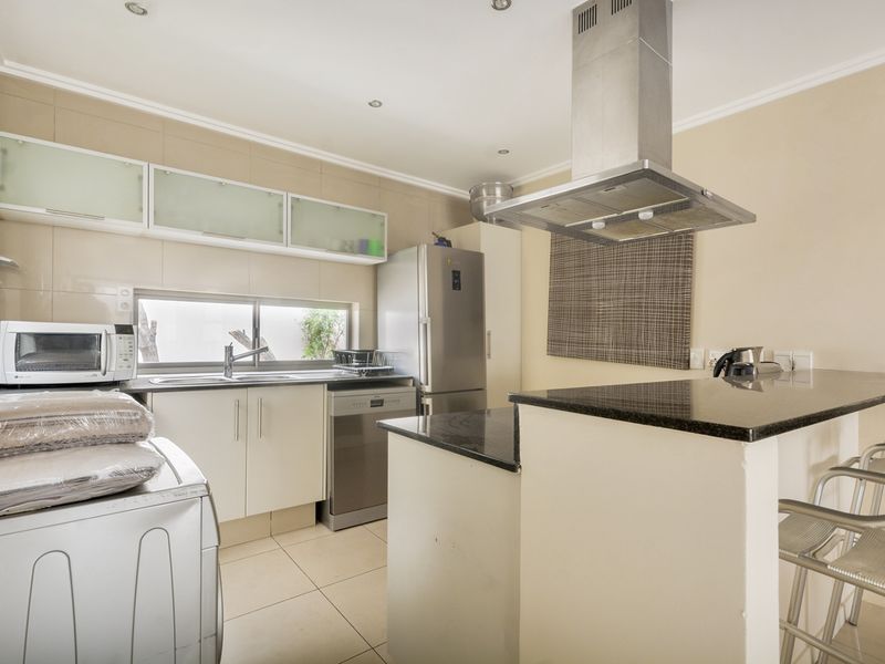 A functional kitchen featuring granite countertops, built-in cabinetry, a stainless steel extractor fan, and tiled flooring, offering a clean and practical workspace.
