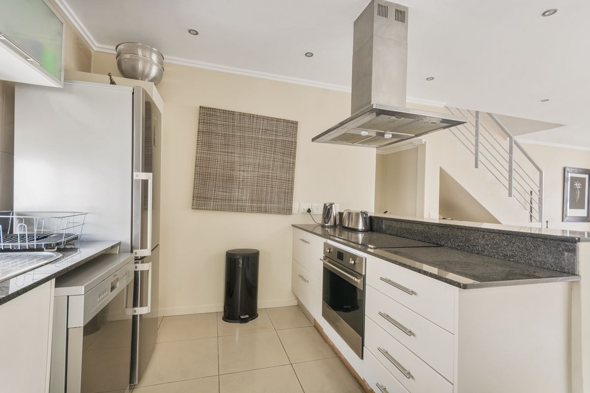 Modern kitchen featuring granite countertops, built-in oven, stainless steel extractor fan, and tiled flooring, with an open-plan layout adjacent to the staircase.