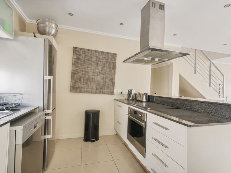 Modern kitchen featuring granite countertops, built-in oven, stainless steel extractor fan, and tiled flooring, with an open-plan layout adjacent to the staircase.