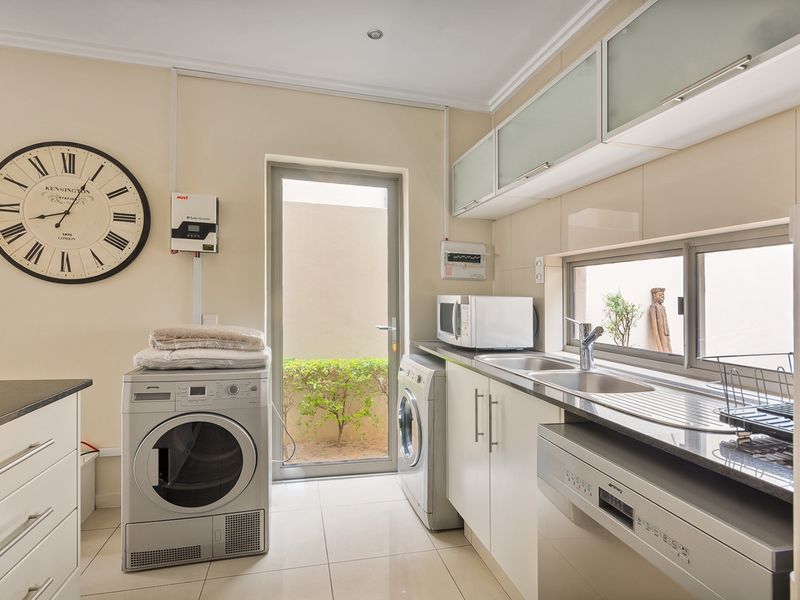 A functional laundry room featuring built-in cabinetry, a stainless steel sink, tiled flooring, and direct access to an outdoor area.
